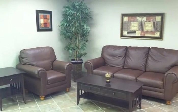 A cozy living room with a brown leather sofa, armchair, coffee table, indoor plant, and wall artwork.