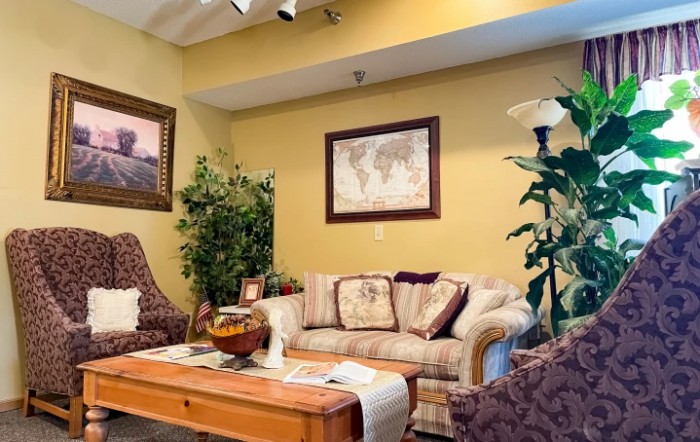 A cozy living room with a sofa, decorative pillows, and plants, featuring a map and artwork on the walls.