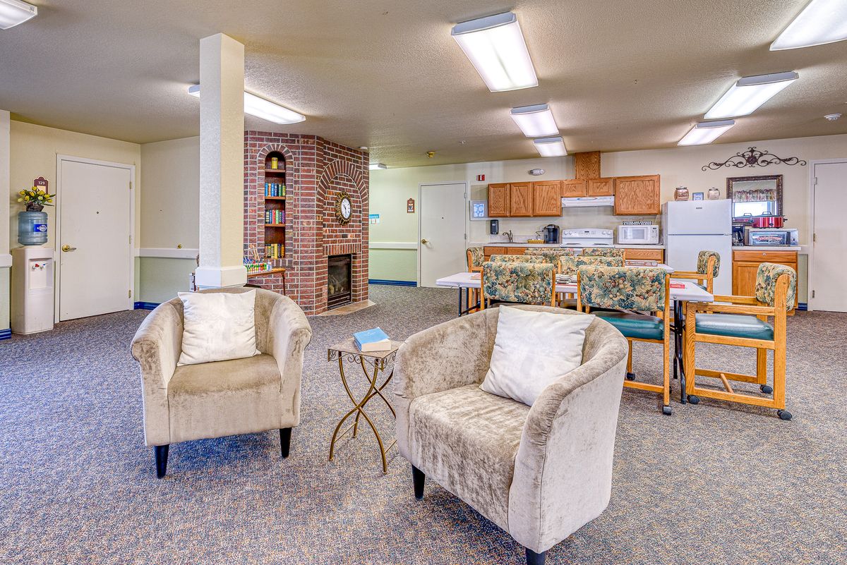 A cozy living room with plush chairs, a small table, and an open kitchen area in the background.
