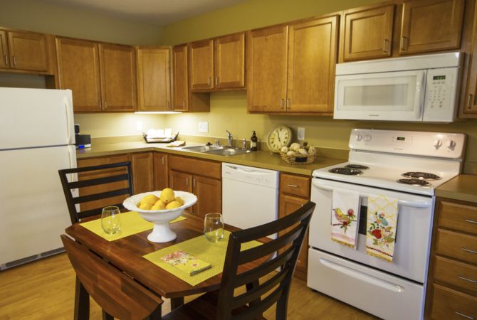 A cozy kitchen with wooden cabinets, a dining table set for two, and modern appliances.