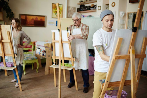 A painting class in progress, featuring an older artist and a younger student focusing on their canvases.
