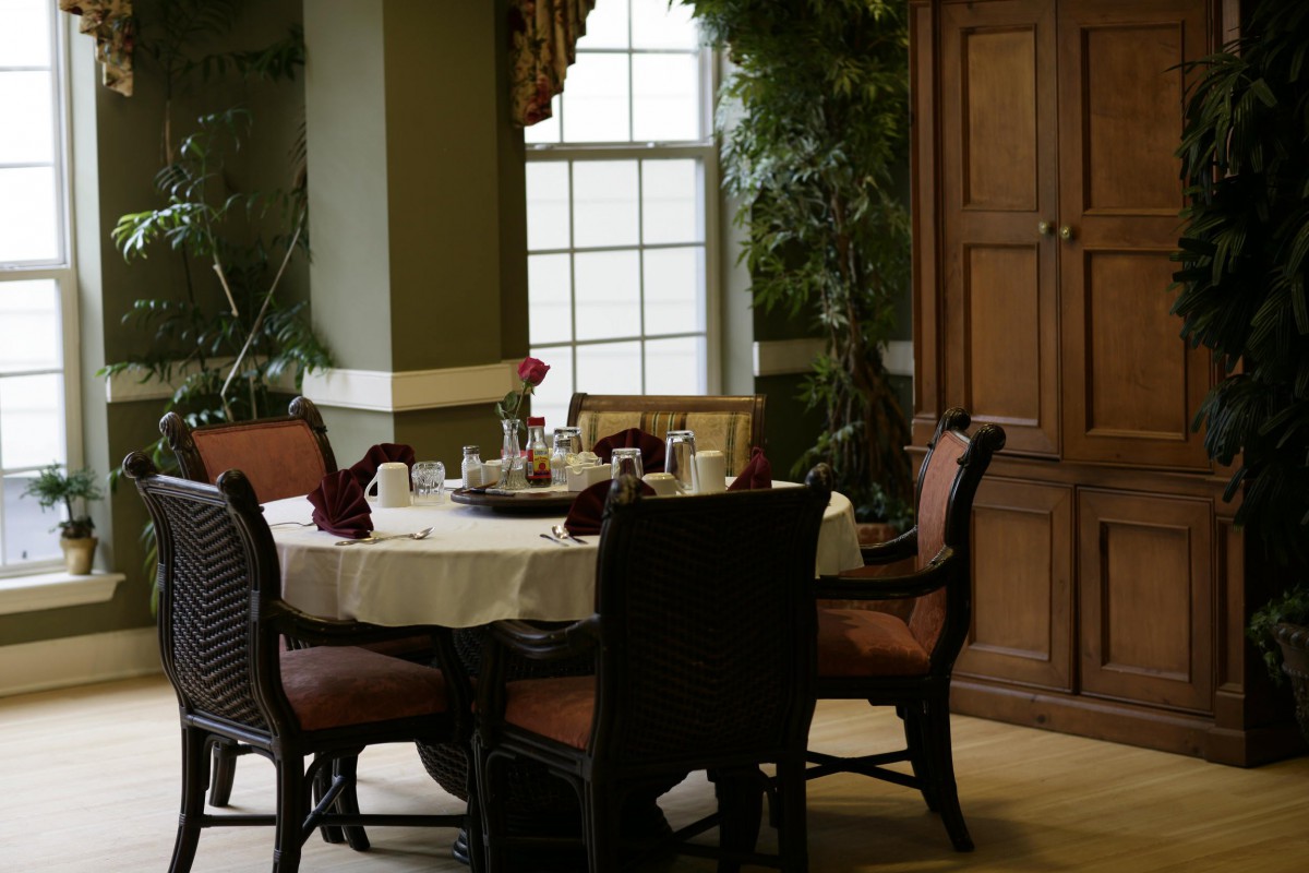 A cozy dining area with a round table set for breakfast, surrounded by chairs and natural light from the window.