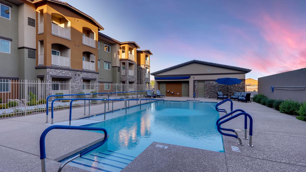 A serene view of an apartment complex with a swimming pool at sunset.