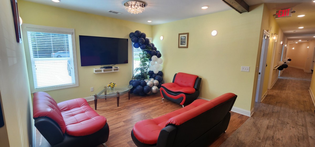 A cozy living room with red and black seating, adorned with a balloon arrangement and featuring a large television on the wall.