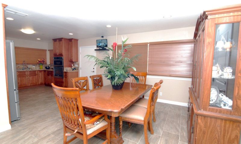 A dining area with a wooden table and chairs, featuring an indoor plant centerpiece, adjacent to a kitchen.