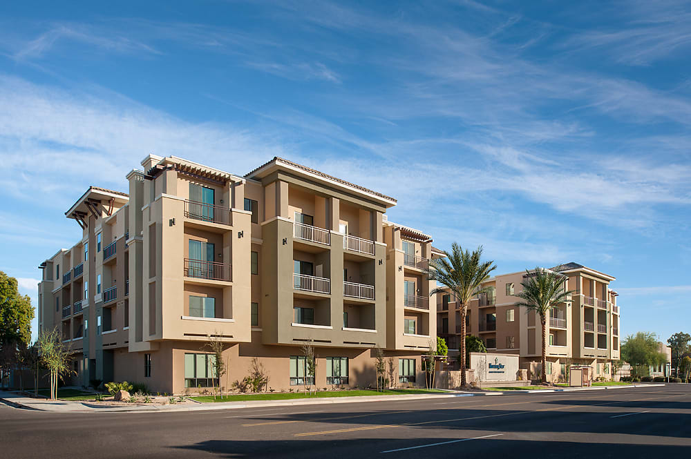 A modern apartment building with balconies surrounded by palm trees and a clear blue sky.