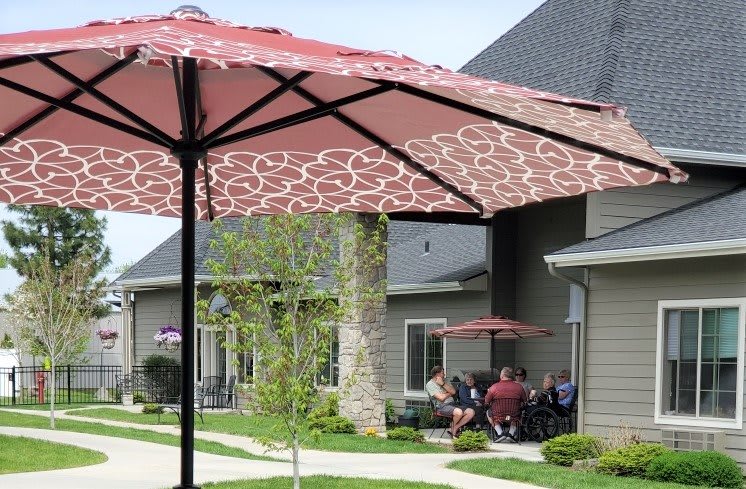 A group of people sitting under a patio umbrella in front of a building.
