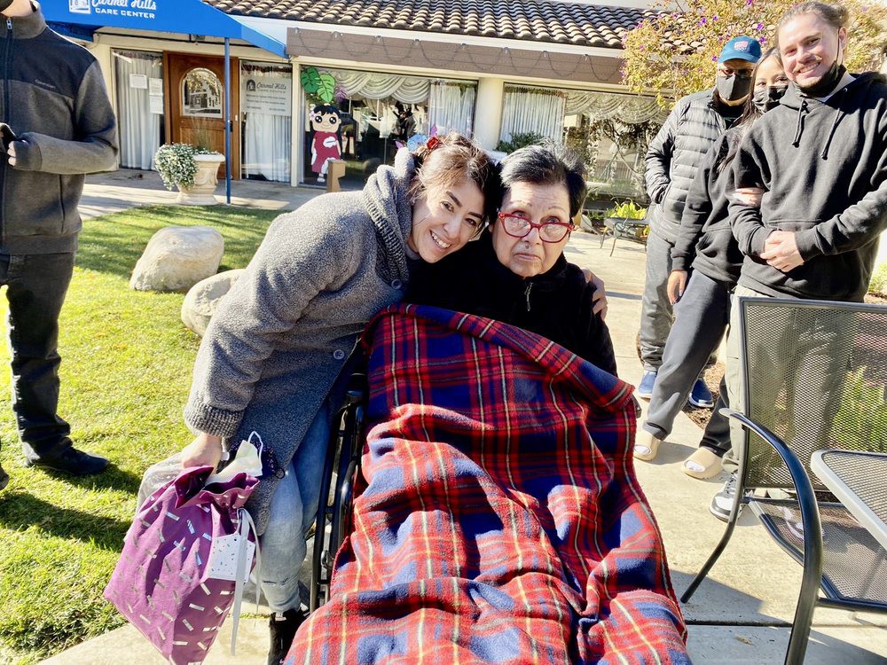 Two people enjoying a sunny day outdoors, one sitting in a wheelchair covered with a blanket.
