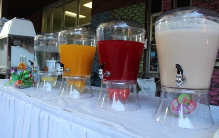 A row of beverage dispensers filled with colorful juices at an outdoor event.