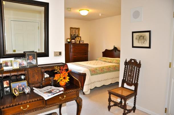A cozy bedroom featuring antique furniture, including a wooden chair, dresser, and a table with a decorative vase.
