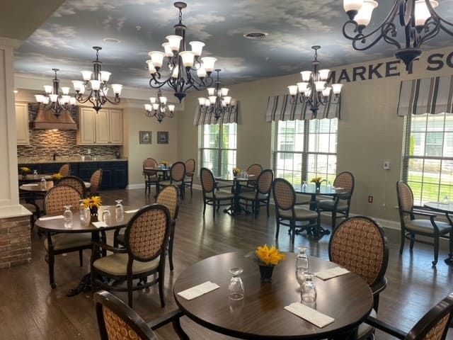 A well-lit dining area with elegant chandeliers, neatly arranged tables, and comfortable chairs.