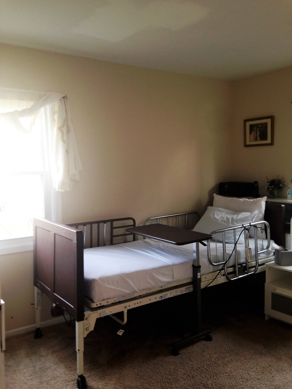 A hospital room with a single bed and medical equipment, illuminated by natural light from the window.