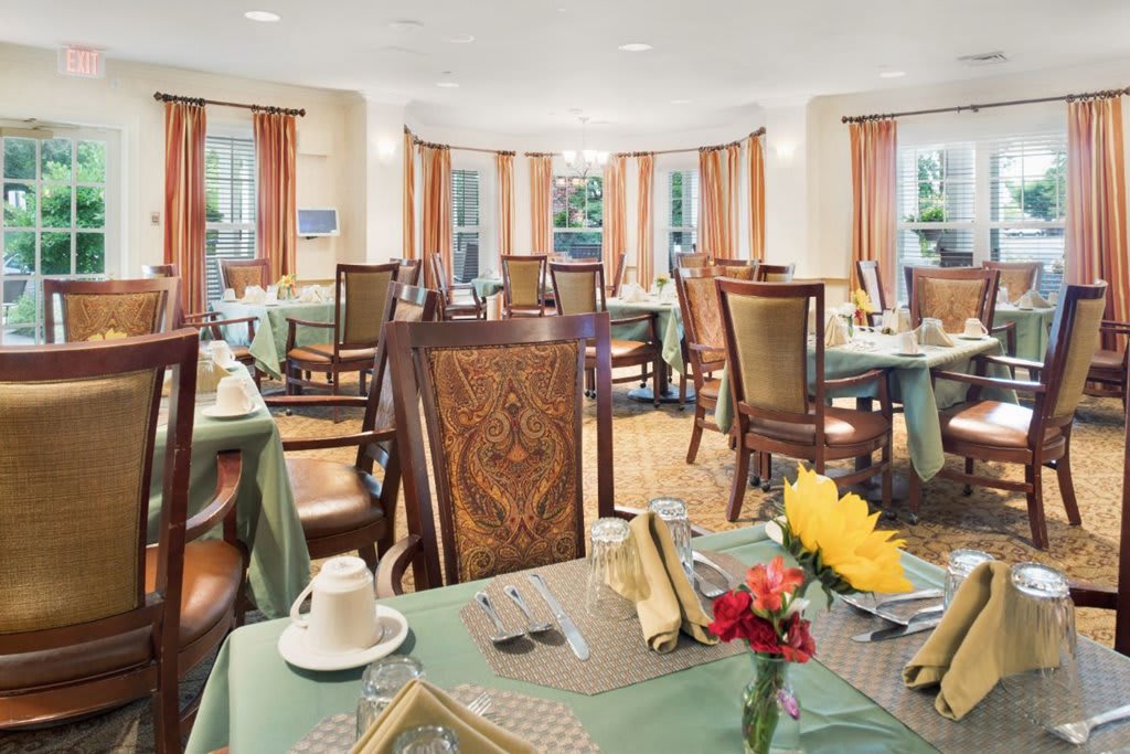 An elegant dining room with neatly arranged tables and chairs, featuring tableware and floral decorations.