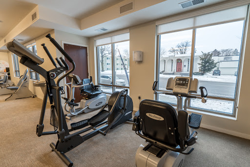 A well-equipped indoor gym featuring an elliptical machine and a recumbent bike, with a snowy landscape visible outside the windows.