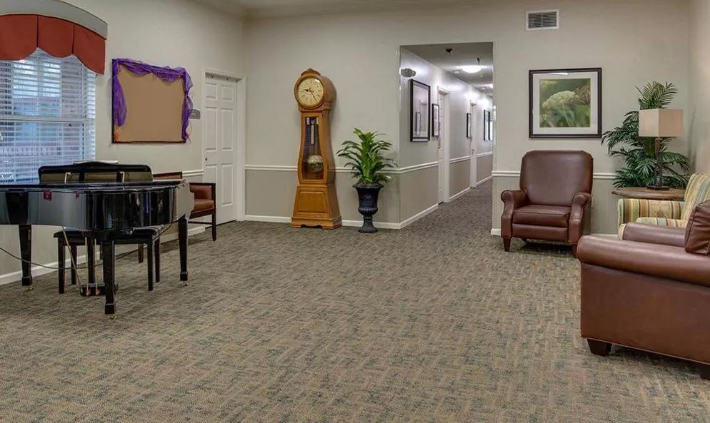 A waiting room with a large clock, seating area, and decorative plants leading to a hallway.