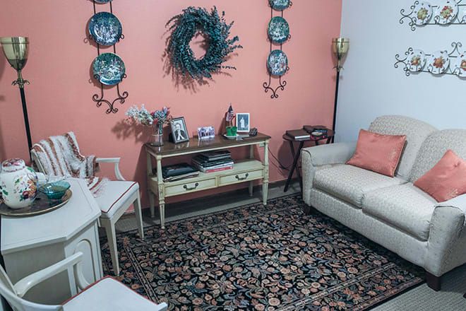 A cozy living room with a decorative wreath and plates on a coral wall, featuring a sofa and a patterned rug.