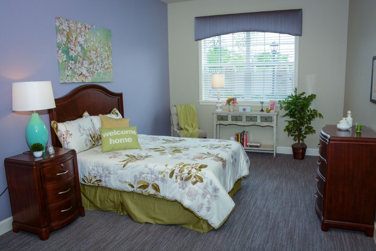 A cozy bedroom with floral bedding, a wooden headboard, and a desk by the window.