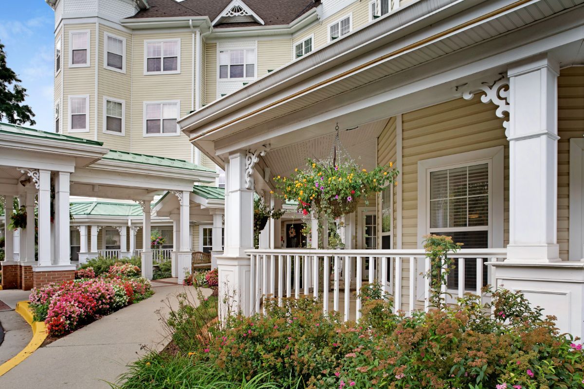 A charming residential building with a spacious porch adorned with hanging plants and surrounded by well-maintained landscaping.