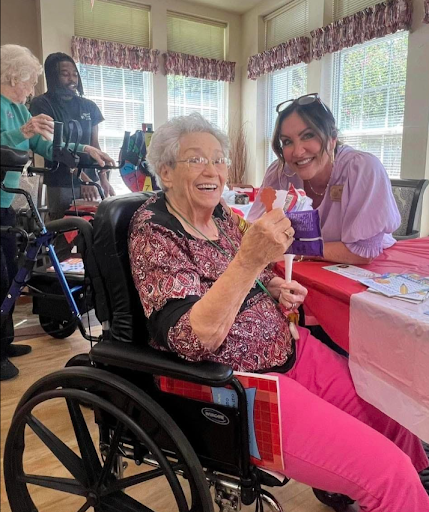 A joyful moment at a community event, where an elderly woman enjoys a treat while being supported by a caregiver.