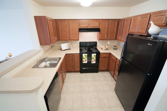 A modern kitchen featuring wooden cabinets, a black oven, refrigerator, and a stainless steel sink.