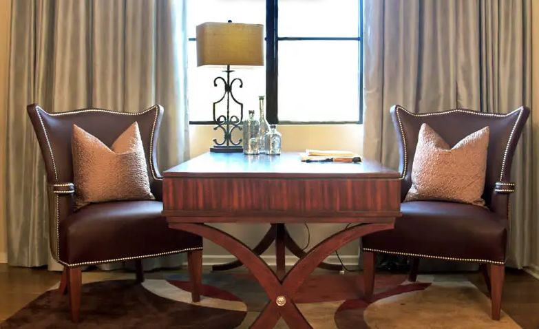 A cozy living room corner featuring a wooden table flanked by two chairs, a stylish lamp, and decorative cushions.