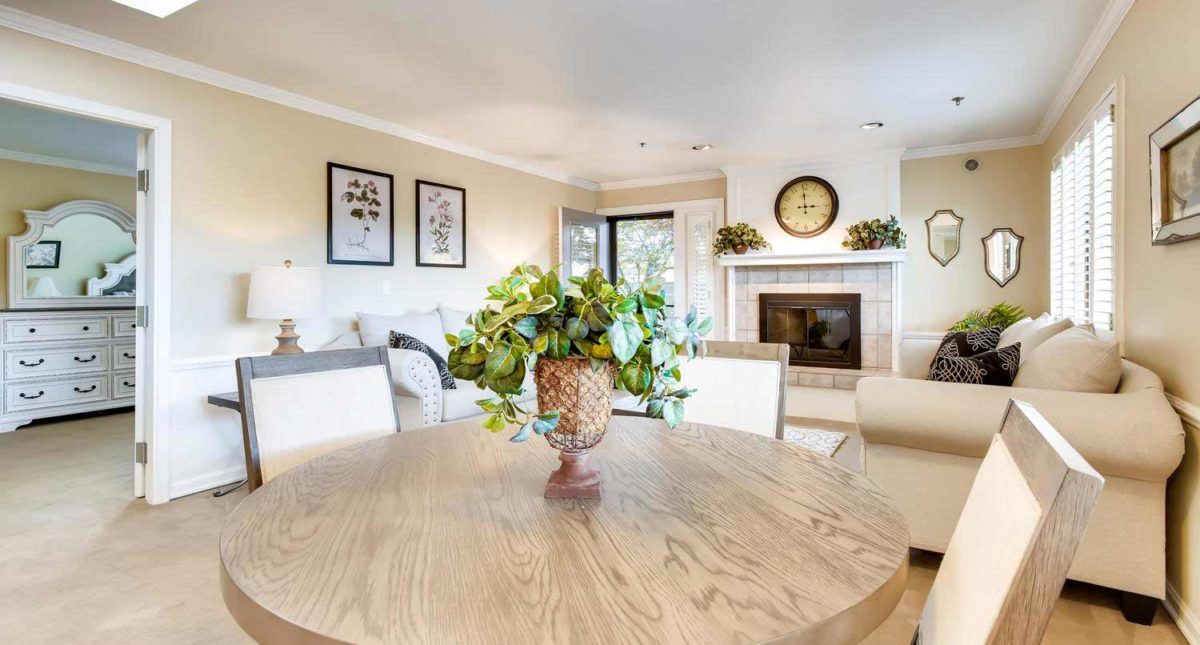 A well-lit living room with a dining area, featuring a round wooden table, chairs, and a fireplace adorned with decorative elements.