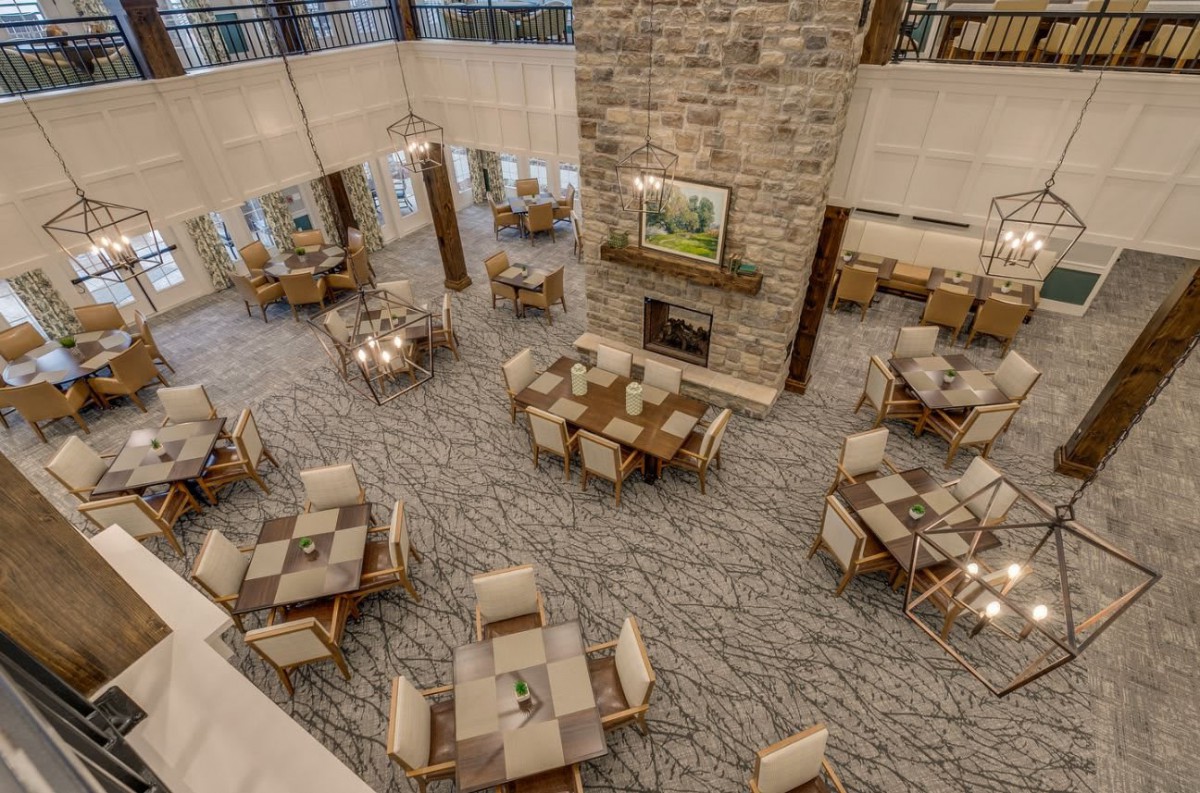 A spacious dining area with multiple wooden tables and chairs, featuring a large stone fireplace.