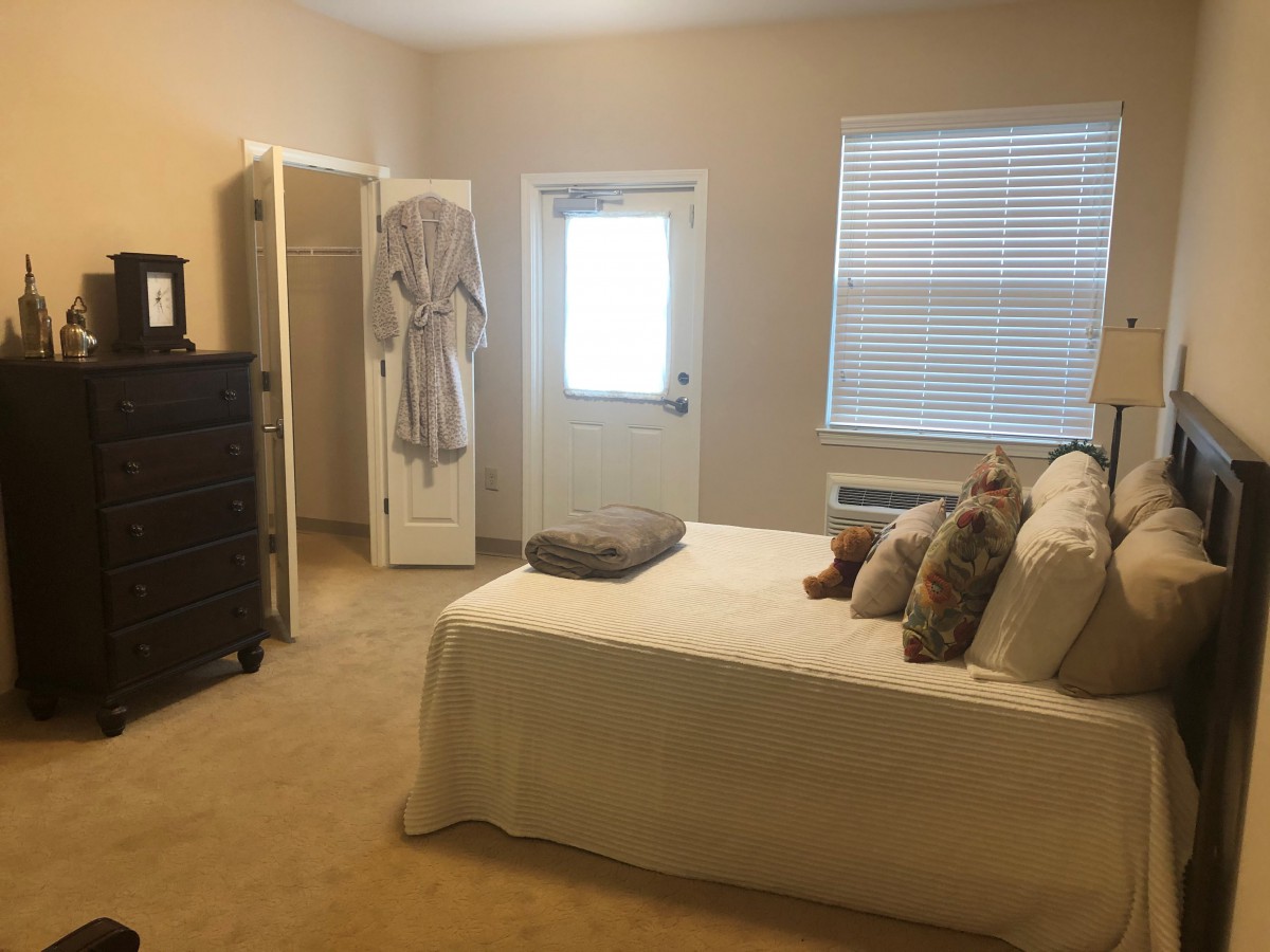 A cozy bedroom with a neatly made bed, dresser, and natural light from the window.