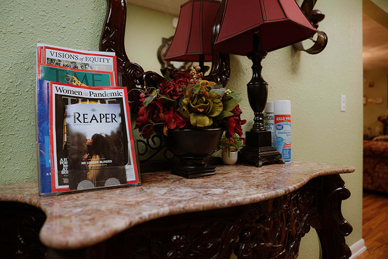 A decorative table with magazines, a lamp, and a floral arrangement.