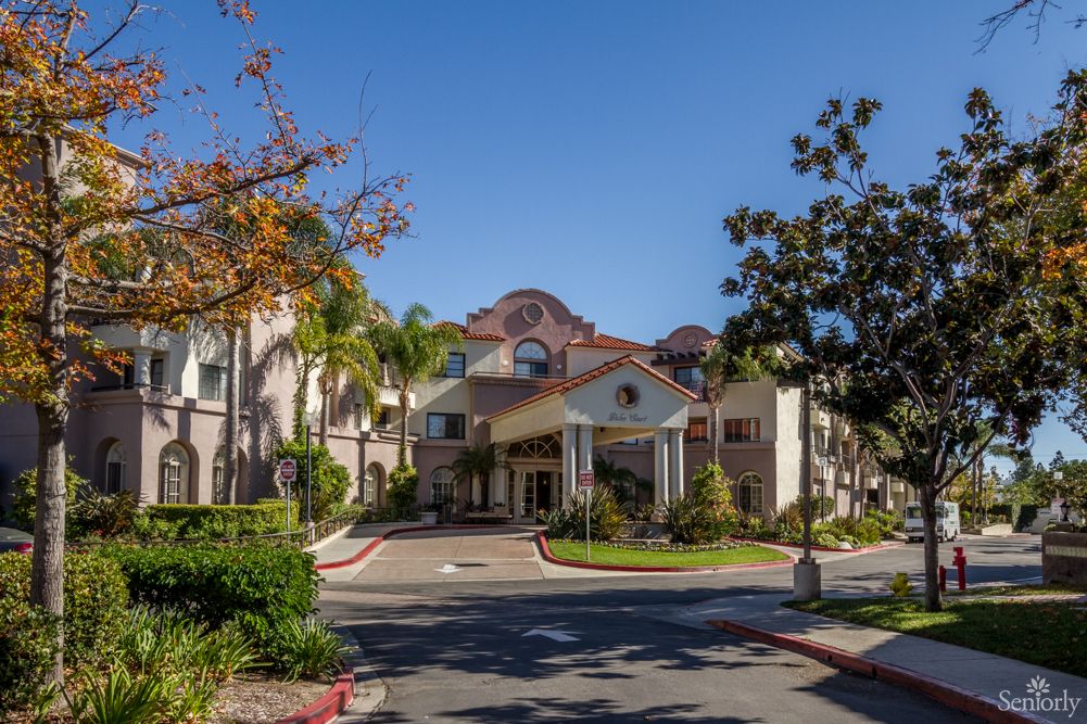 A scenic view of a residential building with a welcoming entrance surrounded by lush greenery and trees on a sunny day.