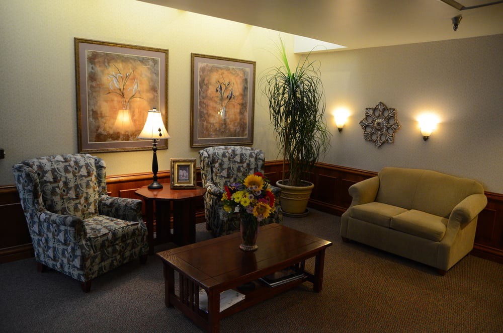 A cozy living room with floral armchairs, a sofa, a wooden coffee table with a vase of flowers, and decorative wall art.