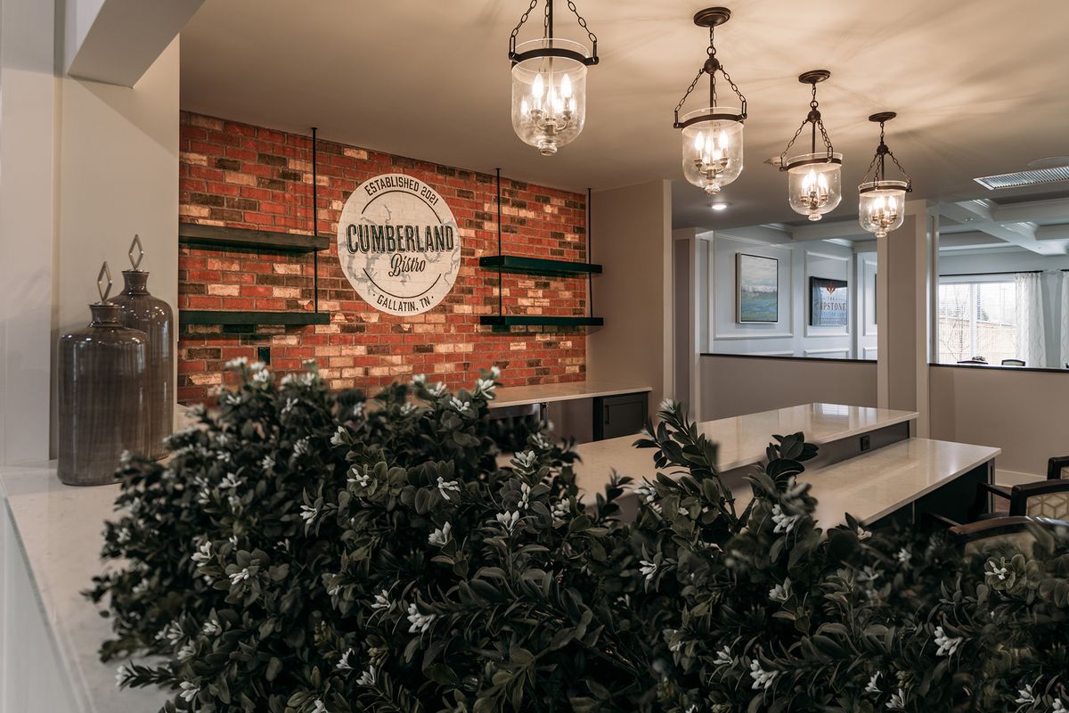 A modern office reception area featuring a brick accent wall with signage, decorative lighting, and lush indoor plants.