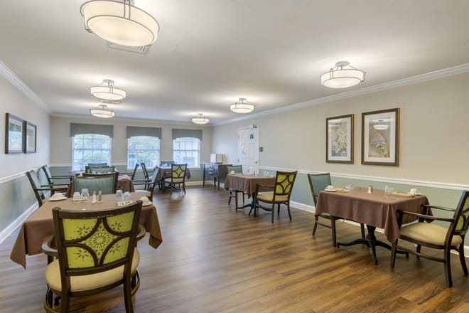 A modern dining room with neatly arranged tables and chairs, warm lighting, and decorative wall art.