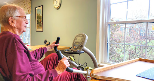 A senior individual exercising on a stationary bike in a well-lit room.