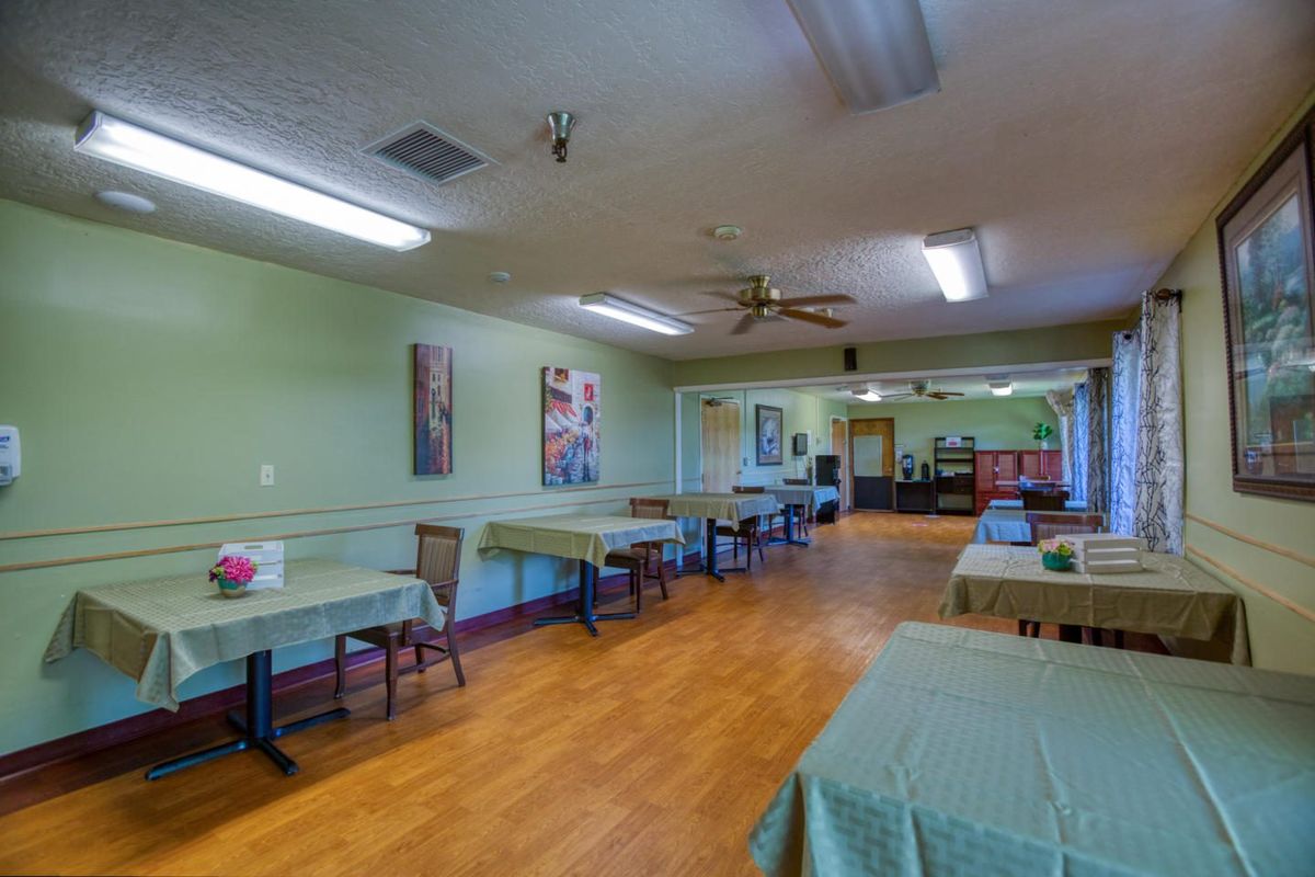 An empty room with green walls, wooden flooring, and tables arranged with chairs.