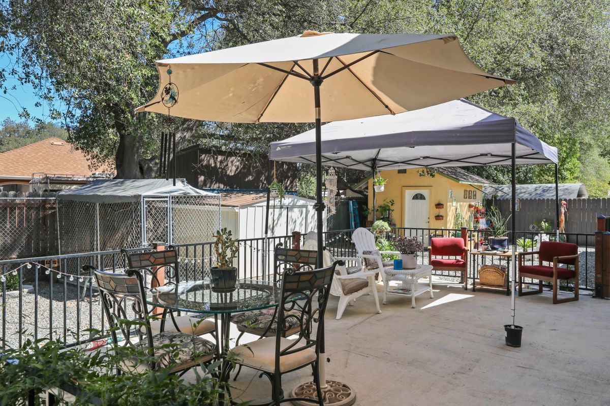 A cozy patio with a table and chairs under an umbrella, surrounded by a lush backyard setting.