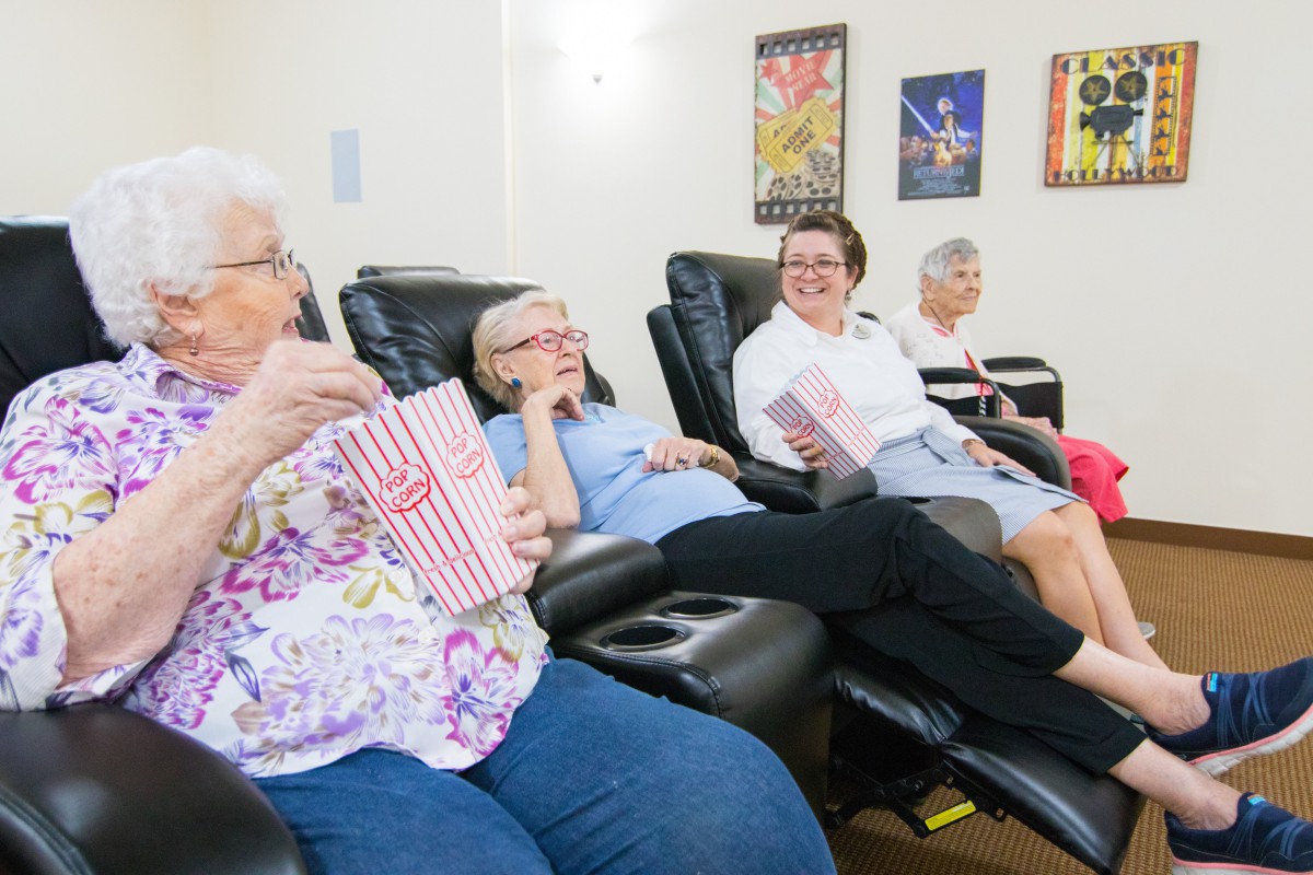 A group of seniors enjoy popcorn while watching a movie together in recliner chairs.