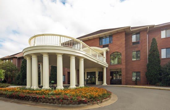 A building with a brick exterior features a grand entrance with columns and well-maintained landscaping.