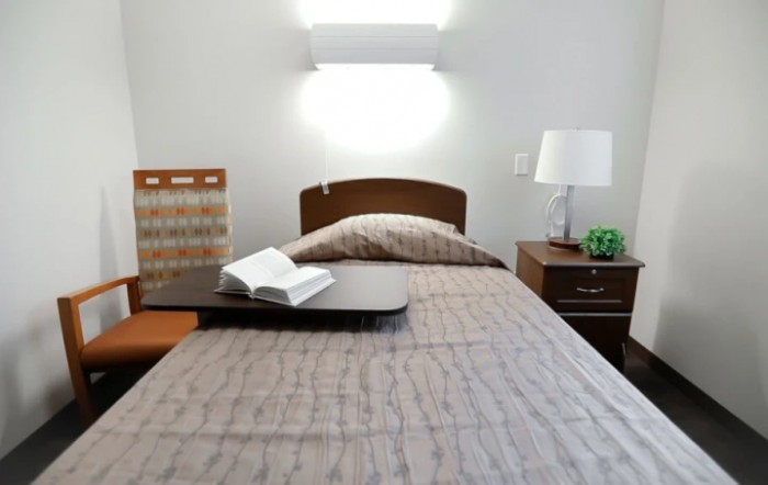 A neatly made bed with a book open on a tray, accompanied by a nightstand and lamp.