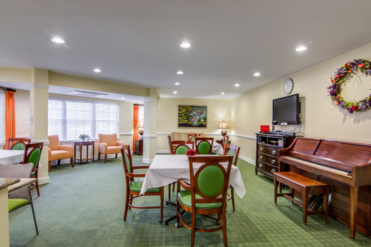A cozy dining area with tables, chairs, a piano, and a television.