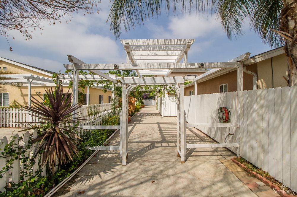 A scenic outdoor walkway with a white pergola surrounded by lush greenery.