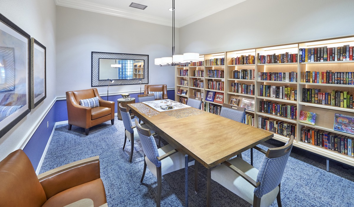 A modern library reading room with a wooden table surrounded by chairs and lined with bookshelves.