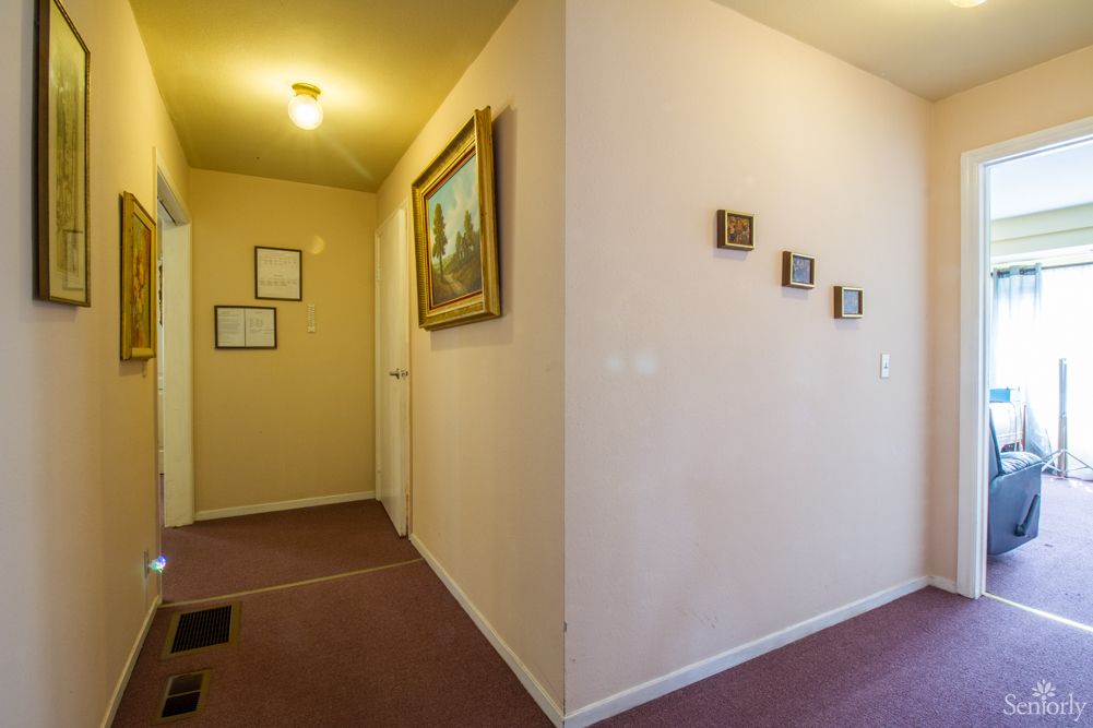 A hallway with artwork on the walls, carpeted flooring, and overhead lighting.