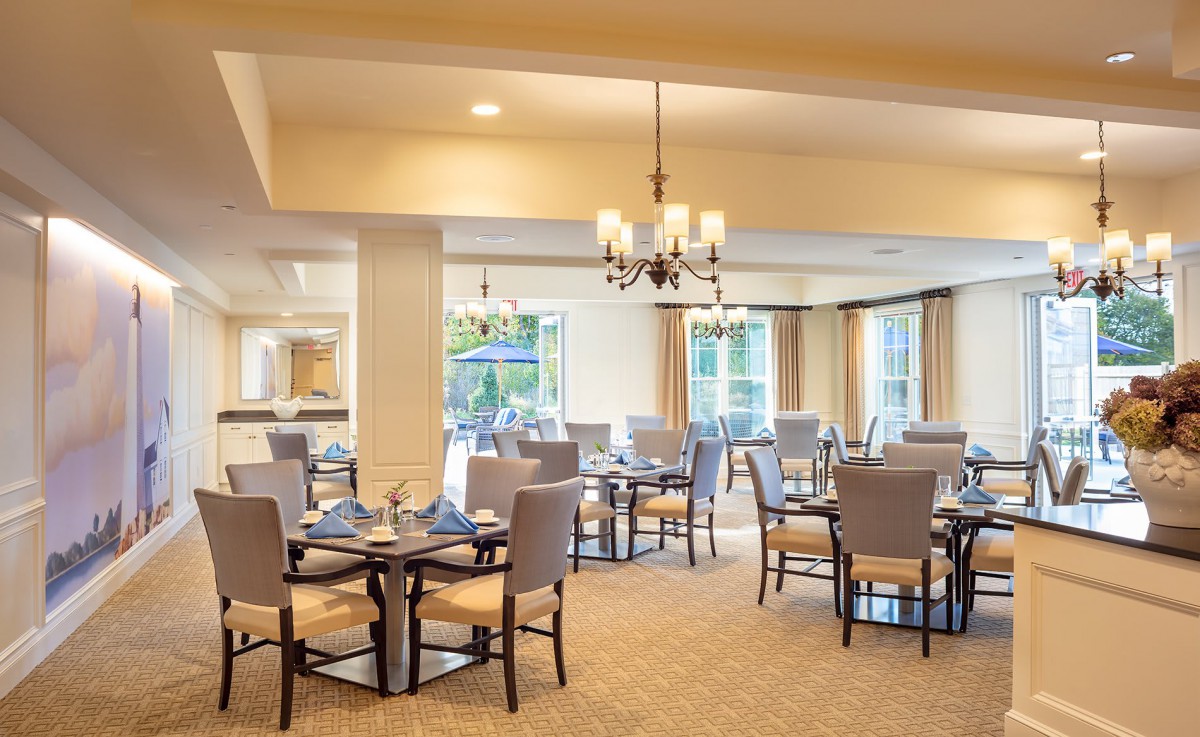 An elegant dining room with neatly arranged tables and chairs, illuminated by a chandelier.