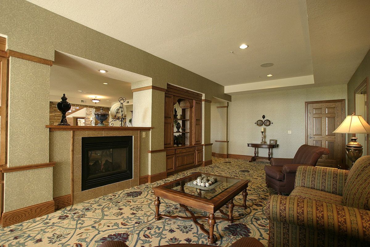 A cozy living room featuring a central fireplace, elegant furniture, and intricate carpet design.