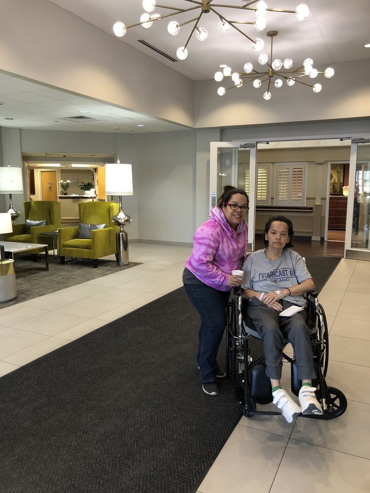 A person in a wheelchair accompanied by another individual in a lobby setting.