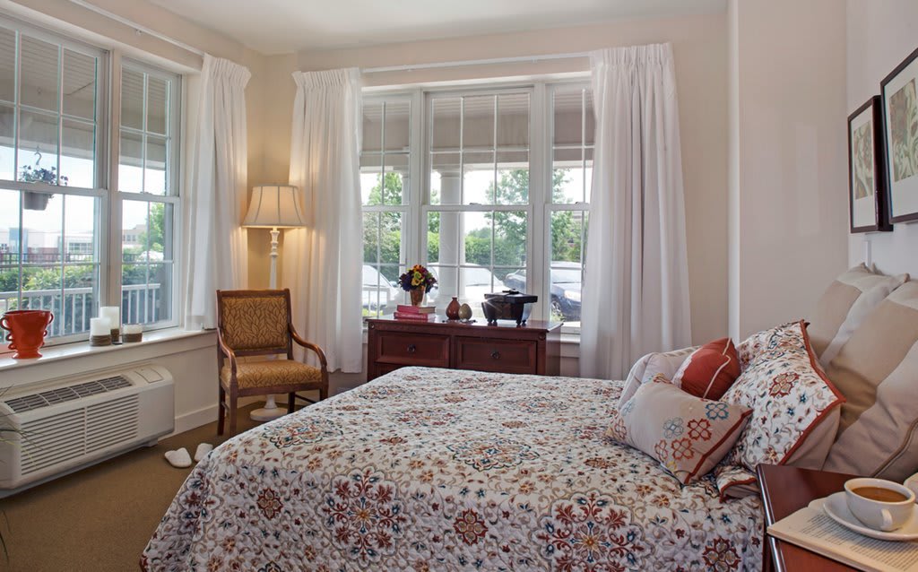 A cozy bedroom with a large window, floral bedding, and classic furnishings.