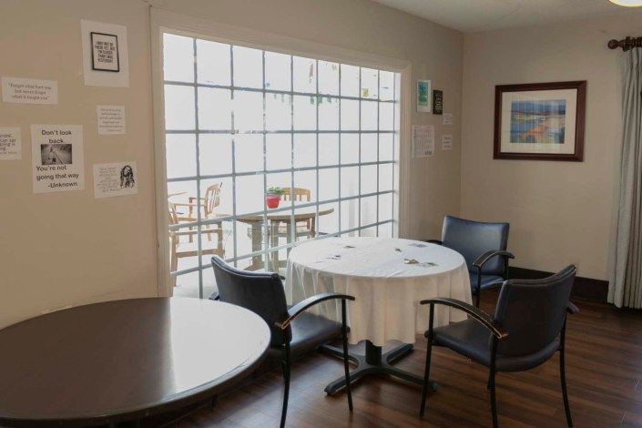 A cozy dining area with round tables and chairs, featuring a large window letting in natural sunlight.
