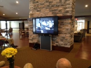 A group of people watching a black-and-white movie on a television mounted on a brick wall in a cozy indoor setting.