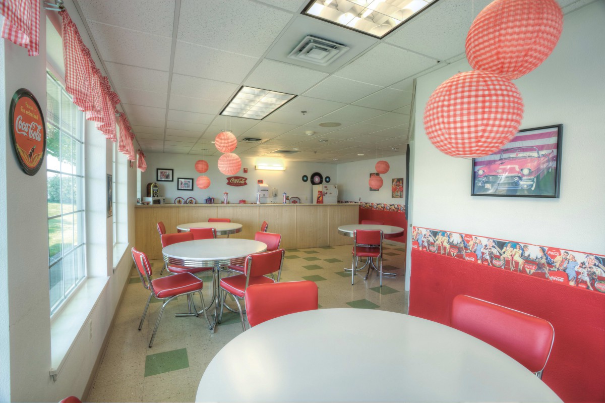 A retro-themed diner with red and white decor, featuring tables, chairs, and hanging checkered decorations.